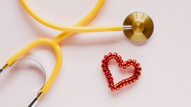 stethoscope near decorative coil tie in heart shape on pink surface